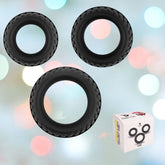 Three black Velv'Or Rooster Floki Silicone Cock Rings of varying sizes are suspended against a blurred background with colorful bokeh lights. In the bottom right corner, there is a white box featuring images of the cock rings and partially visible Velv'Or brand markings.